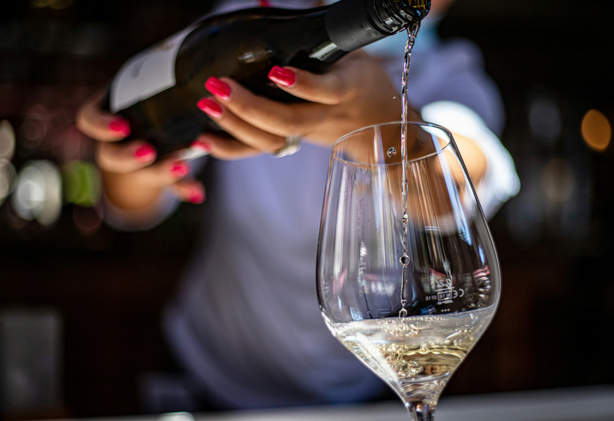 Mulher servindo uma taça de vinho branco Sauvignon Blanc em mesa de restaurante.