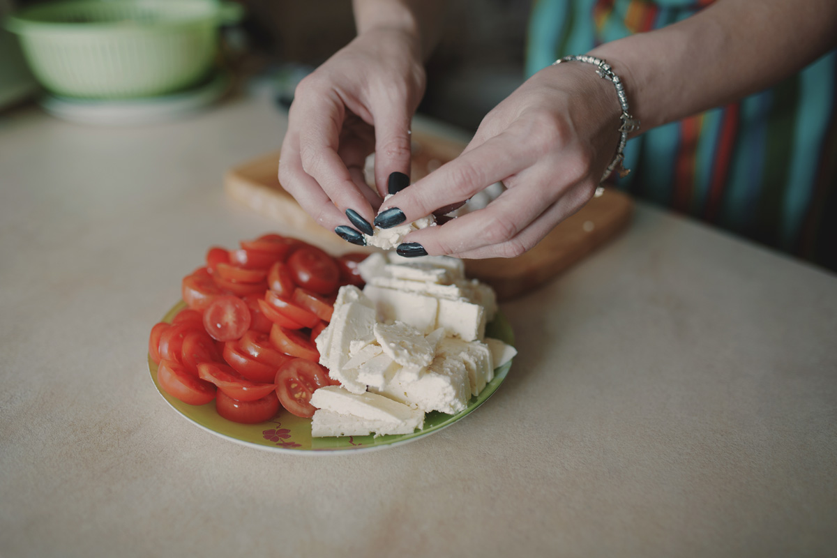 Mãos femininas preparando tábua de frios com queijo e tomate, parte das tradições italianas