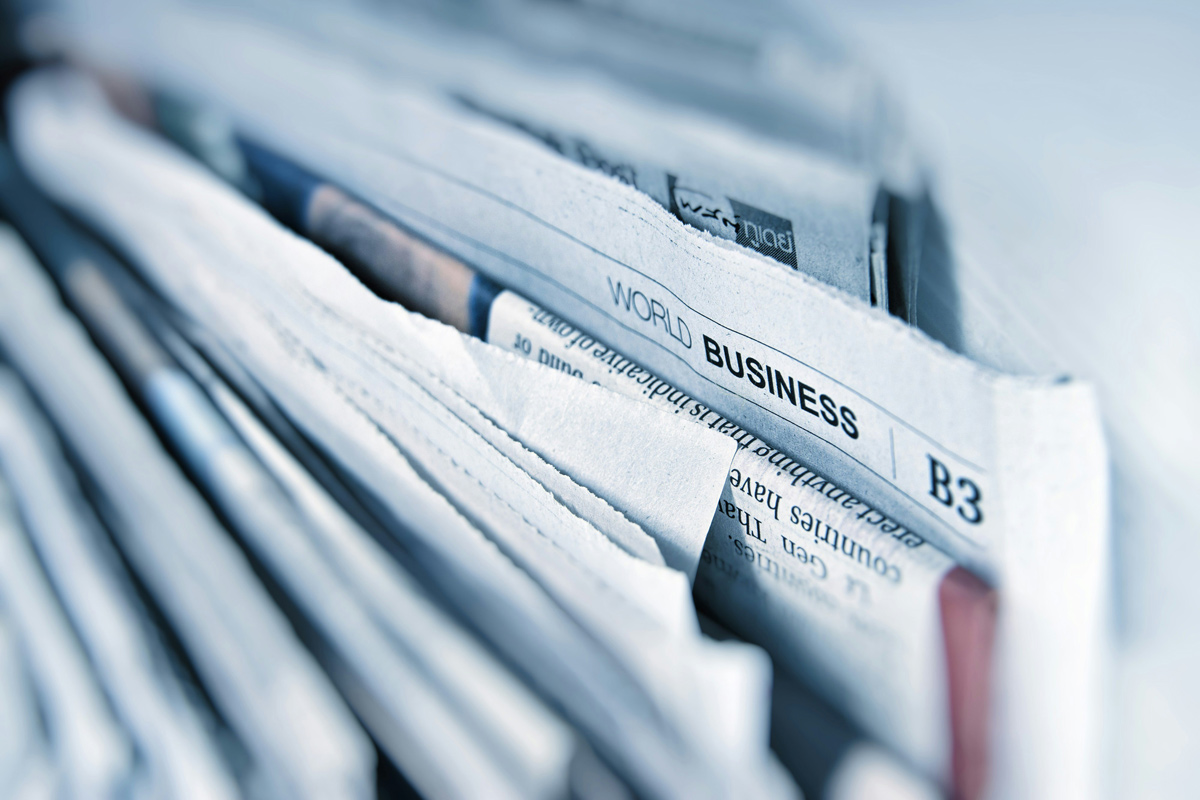 Pilhas de jornais dobrados destacando a editoria de negócios, representando o papel da assessoria de imprensa na visibilidade corporativa.