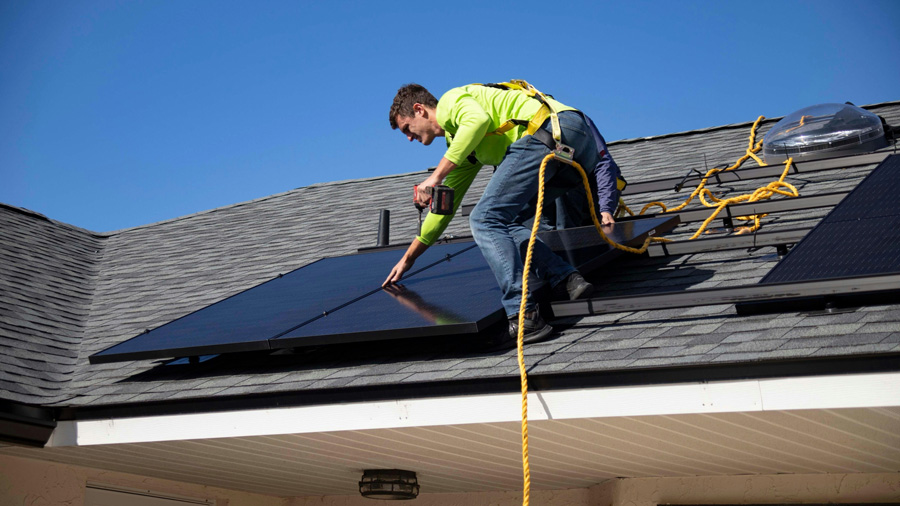 Profissional instalando painel solar em telhado de casa.