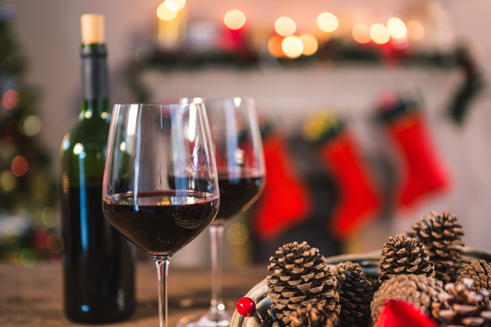 Taças de vinho tinto ao lado de uma garrafa e decoração natalina com pinhas, em um ambiente aconchegante, sugerindo os melhores vinhos para o Natal em uma ceia elegante.