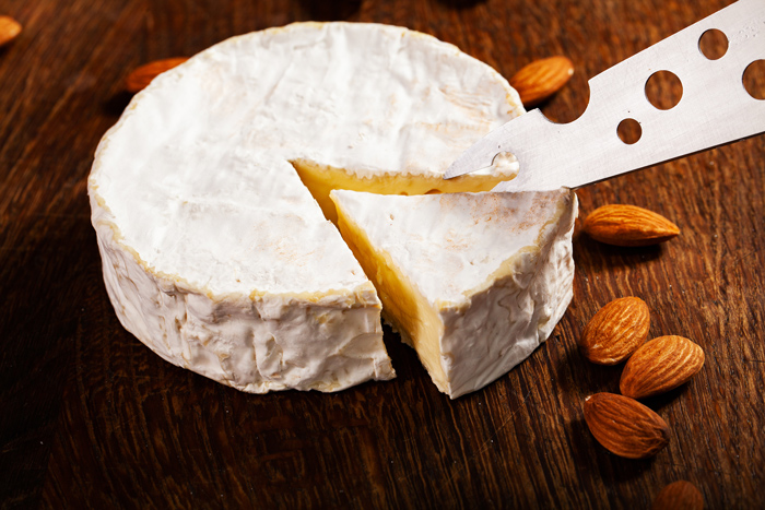 Queijo brie sendo cortado com faca especial, excelente opção de vinho com queijo suave.  