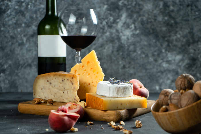 Tábua com queijos variados, frutas e taça de vinho tinto, formando uma mesa de queijos e vinhos completa. 