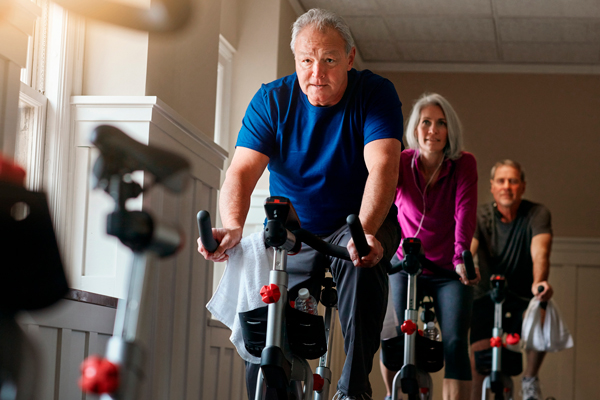Grupo de pessoas acima dos 50 anos praticando spinning em academia com bicicleta ergonômica indoor. 