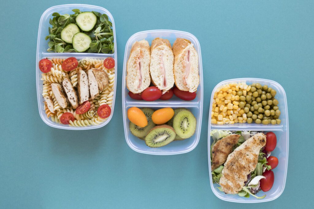 Marmita com alimentos congelados saudáveis, incluindo sanduíches integrais, frutas e vegetais frescos, ilustrando que comida congelada não faz mal quando bem preparada e armazenada.