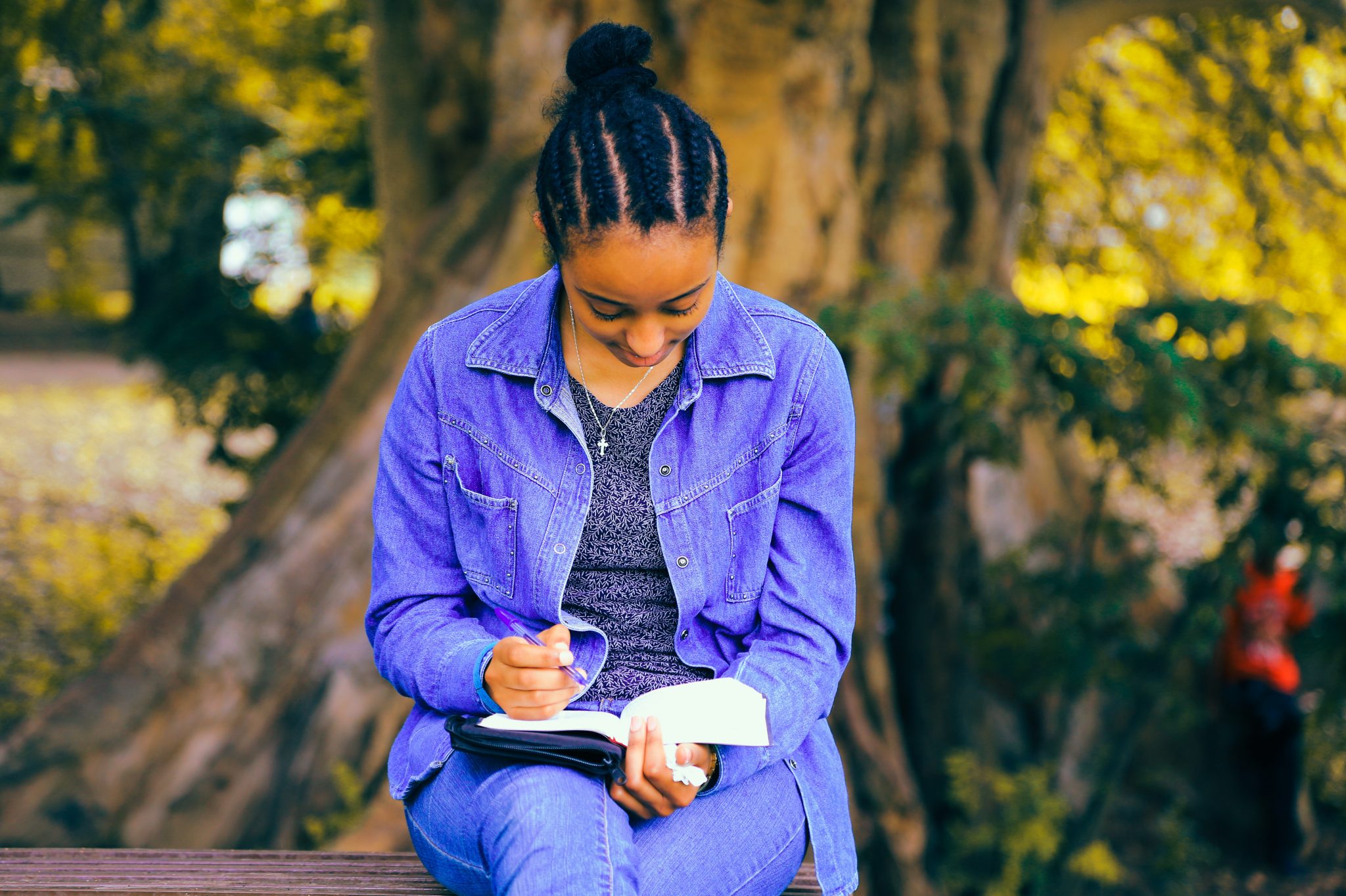 Mulher sentada em banco de praça lendo livro de escritora negra e fazendo anotações.