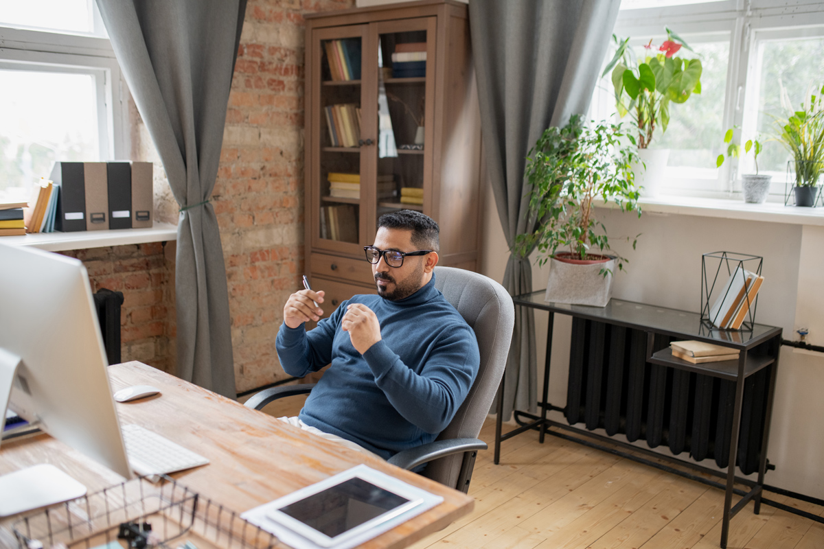 Profissional em home office gesticulando durante uma call, mesa organizada e plantas ao fundo